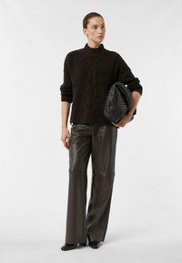 Dark brown knitted sweater with high neck and cable pattern, paired with olive green leather wide-leg pants and a textured black handbag.