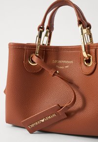Brązowa torba Emporio Armani z teksturowanej skóry, z złotymi okuciami, podwójnymi uchwytami i przymocowaną skórzaną metką z logo.
