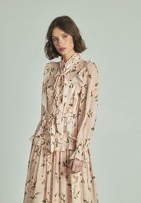 Vestido de estampado floral en suave tono rosa, con volantes, mangas largas y cintura ceñida con cinturón. Elaborado en una tela ligera y fluida.