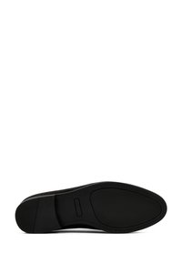 Chaussure en daim noir avec un bout rond, semelle en caoutchouc et accents en cuir lisse contrastants le long des bords. Fini texturé sur la semelle.