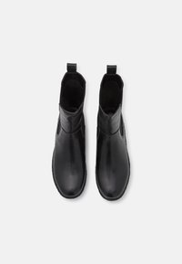 Botas negras hasta el tobillo de cuero suave, con un tobillo alto, lengüetas para facilitar el calzado y sin cierres visibles. Diseño simple y elegante.