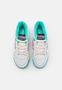 Valkoiset lenkkitossut, joissa turkoosit yksityiskohdat, vaaleanpunaiset raidat ja teksturoitu yläosa. Varustettu pehmustetulla kauluksella ja kermaisilla nauhoilla. Adidas-logo näkyvästi esillä.