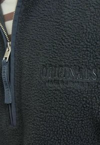 Fleecejakke i mørkegrå, med lynlås foran, struktureret overflade og broderet "ORIGINALS" logo på brystet.