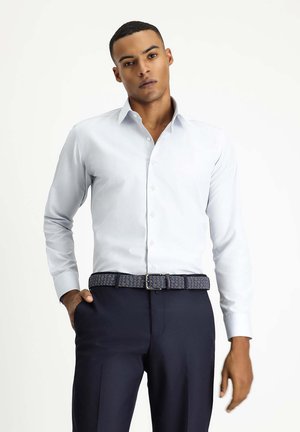 Camisa de manga larga azul claro con cierre de botones, combinada con pantalones oscuros y un cinturón tejido de diseño. Tejido suave con un corte entallado.