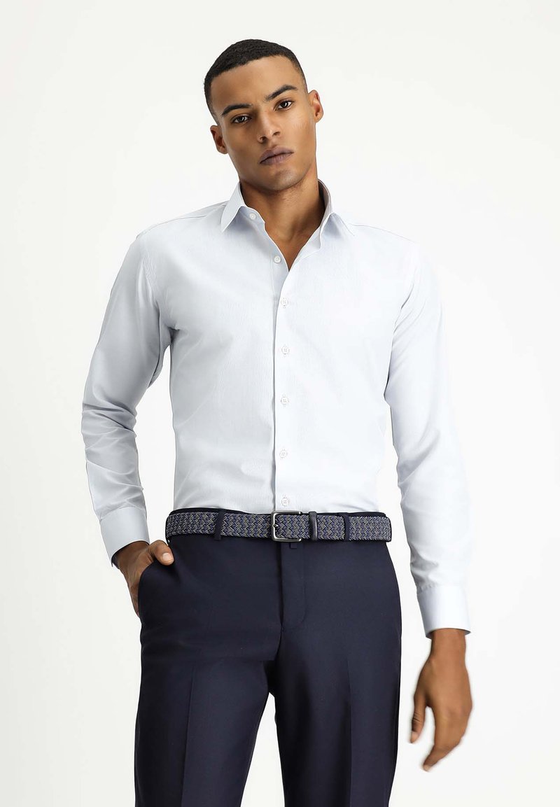 Camicia azzurro chiaro a maniche lunghe con chiusura a bottoni, abbinata a pantaloni scuri e una cintura intrecciata a motivo. Tessuto morbido con vestibilità su misura.