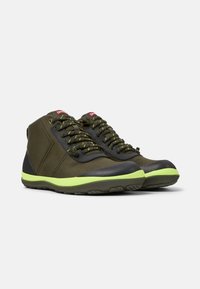 Zapatillas altas de color verde oscuro con acentos negros, tela texturizada, costuras reflectantes y una suela de goma de color verde brillante.