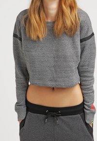 Grå kortärmad sweatshirt med lång ärm, med svarta ränder på axlarna. Tillverkad av mjukt tyg, i kombination med mörkgrå byxor med dragsnöre.