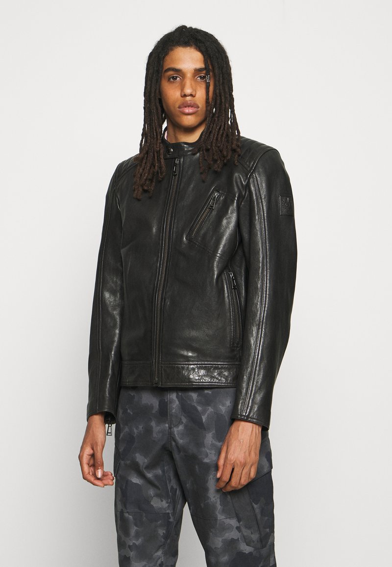 Black leather jacket with a stand collar, zip front, and slim fit. Features one chest pocket and a textured finish. Styled with camouflage pants.
