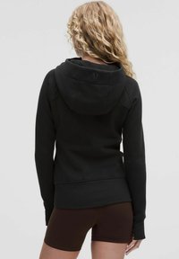 Black hooded sweatshirt with a fitted design, featuring a stitched seam detail, and a discreet logo on the back. Paired with brown shorts.