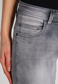 Jeans de denim gris con un leve desgaste, que presentan un diseño estándar de cinco bolsillos, una cinturilla cosida y una silueta ajustada.