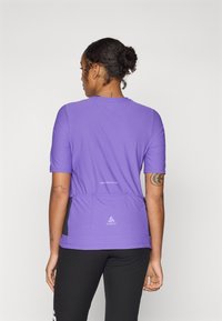T-shirt de sport violet à manches courtes, avec une coupe ajustée et une ceinture noire contrastante. Détails du logo et du texte au dos.
