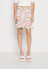 Jupe fleurie avec un fond bleu clair, des roses roses, un ourlet à volants et une taille ajustée. Associée à des sandales à talons blocs roses brillantes.