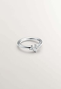 Anillo de plata con tres piedras claras y brillantes en un engaste de racimo sobre una banda lisa. Superficie reflectante con un acabado pulido.