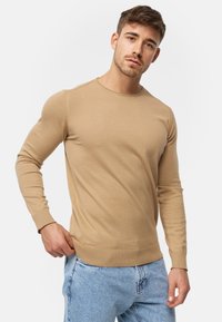 Beige langærmet sweater lavet af strikstof, med rund halsudskæring og ribbede manchetter, parret med lysblå denim jeans.