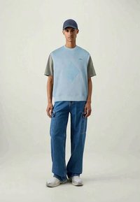Top azul claro sem mangas com um design texturizado em forma de diamante, combinado com jeans largos azuis com bolsos tipo cargo e ténis brancos.