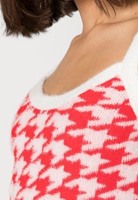 Červený a bílý pletený top bez rukávů s motivem pepita, jemnou texturou a širokým výstřihem s kontrastním bílým lemováním.