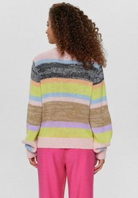 Nertinis megztinis su daugiaspalvėmis horizontaliomis juostelėmis pastelinių atspalvių, laisvos formos ir su sukrautais rankogaliais, derinamas su rožinėmis kelnėmis.