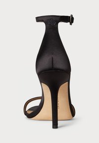 Melna satīna augstpapēžu sandaļa ar norādītu purngalu, plānu potītes siksniņu un šauru stiletto papēdi. Rīkojas ar teksturētu iekšējo zoli.