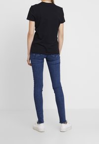 Camiseta de algodón negra de manga corta, combinada con jeans ajustados azules con un ligero deshilachado en el dobladillo y zapatillas blancas.