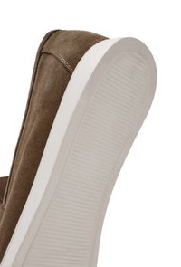 Zapato sin cordones de ante marrón con una suela de goma blanca. Presenta una suela texturizada con estrías verticales y costuras reforzadas a lo largo del borde superior.