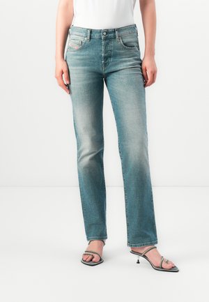 Light blue straight-leg jeans made of denim, featuring five pockets, subtle fading, and contrast stitching. Paired with silver heeled sandals.