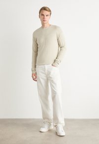 Maglione lavorato a maglia beige con scollatura rotonda, caratterizzato da un logo sottile; abbinato a pantaloni bianchi larghi e sneakers bianche. Tessuto morbido.