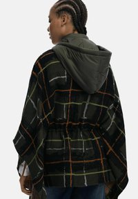 Kariertes Poncho in Dunkelgrün mit orangefarbenen, weißen und grauen Linien; verfügt über eine abnehmbare, grüne, gepolsterte Kapuze; lockere Passform und strukturierten Stoff.