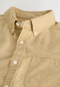 Chemise à carreaux beige et marron avec des boutons, col boutonné et poche poitrine.