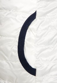 Tissu isolant blanc avec un accent en tissu bleu marine formant une ouverture circulaire. La texture semble lisse et gonflée.