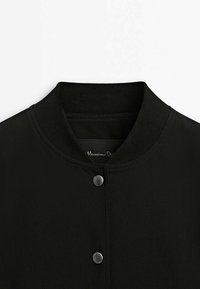 Veste bomber noire avec col côtelé et boutons-pression, montrant les détails du devant supérieur et de l'encolure.