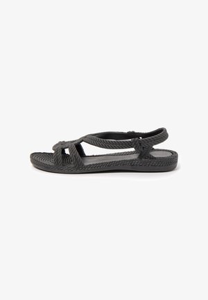Black braided flat sandal with open toe, adjustable back strap, and textured sole, shown from the side on a white background.