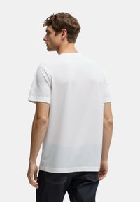T-shirt bianco a maniche corte con collo a giro, texture liscia e senza motivi visibili, indossato con jeans di denim scuro.
