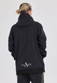 Zwarte hoodie-jack met hoge kraag en ritssluiting. Heeft een wit logo op de achterkant en elastische manchetten. Glad, matte textuur.