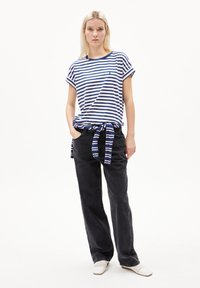 Striped cotton t-shirt in blue and white, relaxed fit, cuffed sleeves, paired with high-waisted black denim pants and white woven shoes.