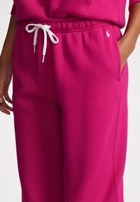 Fuchsiarosa sweatpants med dragsko i midjan, utrustade med sidofickor och en broderad logga på vänster sida. Mjuk textur, avslappnad passform.