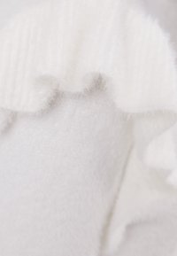 White knitted fabric featuring a soft, fluffy texture with a ribbed pattern at the edge, creating a wavy, layered appearance.
