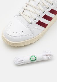 Vita lädersneakers med röda tygremsor, rund tå och perforerade detaljer. Inkluderar vita snörningar med en logotagg.