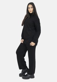 Maglione nero lavorato a maglia con collo alto e pannelli laterali testurizzati, abbinato a pantaloni neri lavorati a maglia coordinati e scarpe nere chunky.