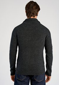 Donkergrijze gebreide trui met een sjaalkraag, geribbelde boorden en zoom, en een zachte textuur. Gezien van achteren, met blauwe spijkerbroek zichtbaar.