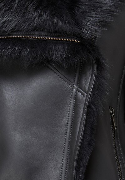Crna kožna jakna s mekim crnim krznom, izloženim patentnim zatvaračem i detaljno šivenjem na koži. Vidljive teksturirane kontraste.