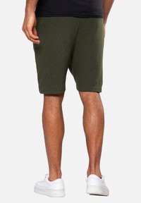 Shorts verts côtelés en matériau doux, arrivant aux genoux, avec une taille élastique, accompagnés de baskets blanches.