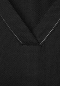 Schwarzer Stoff mit V-Ausschnitt-Design, das strukturiertes Material und kontrastierendes weißes Nähen entlang des Ausschnitts aufweist.