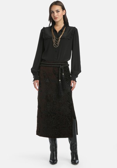 Črna bluza z dolgimi rokavi in nabranim ovratnikom, v kombinaciji z temno, teksturirano krilo, ki ima cvetlični vezenin in pas s resicami.