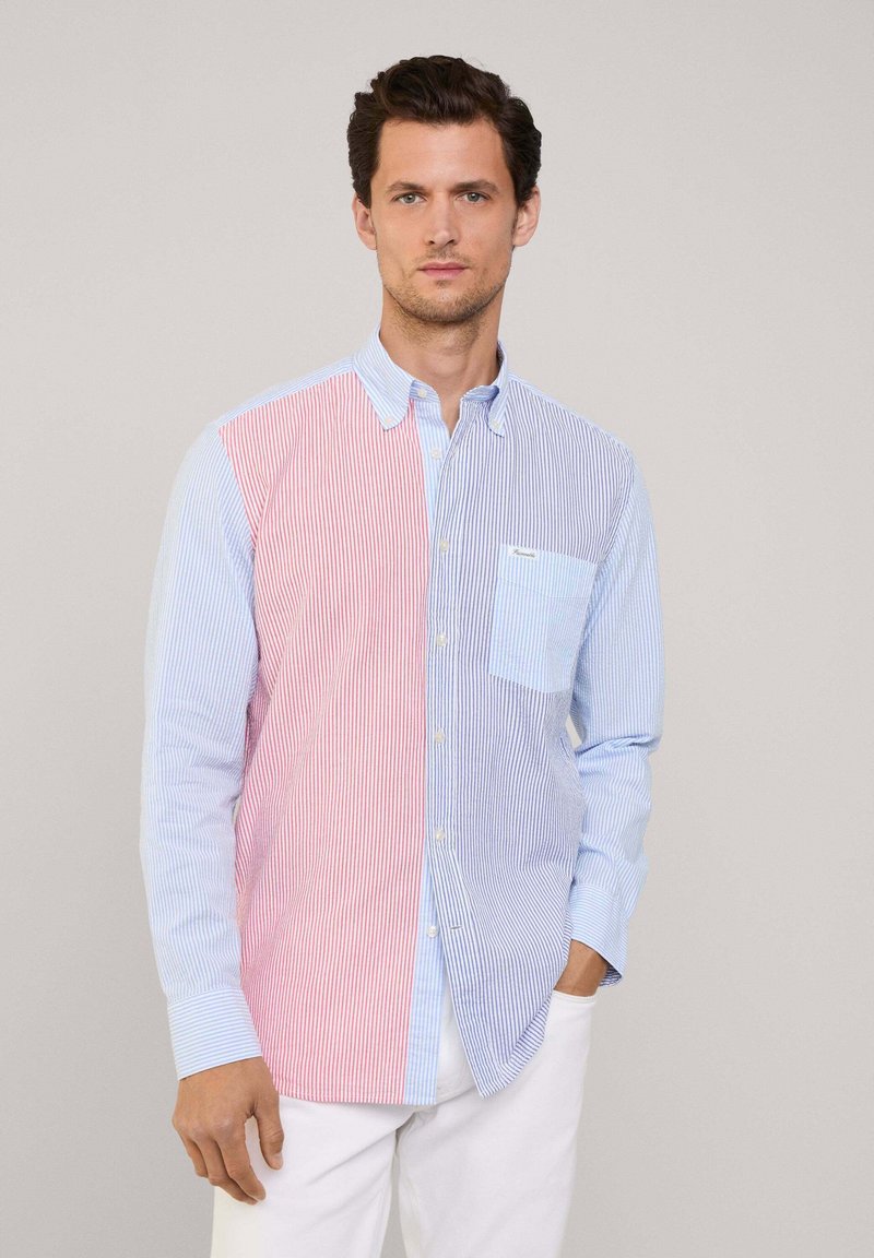 Camisa abotonada con rayas verticales; lado izquierdo rojo y blanco, lado derecho azul claro y blanco. Tiene un bolsillo en el pecho y un cuello.