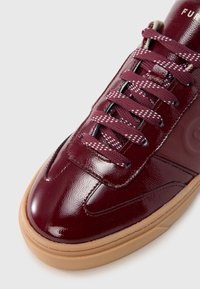 Sneakers i burgunderfarget lakkskinn med rund tupp, lagdelt gummisåle og kontrasterende snører med hvite prikkemønster. Fremhevet logo på tungen.