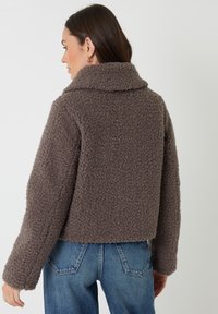 Brun, fluffy, tekstureret cropped jakke med bred krave og sænkede skuldre, parret med højtaljede blå jeans.