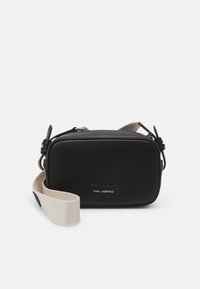 Svart læder crossbody taske med rektangulær form, udstyret med en stofrem og en metal lynlås. Etikett detaljer på forsiden.