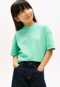 Βαμβακερό t-shirt σε μέντα πράσινο χρώμα με το λογότυπο "HILFIGER" σε άσπρο, συνδυασμένο με σκούρα μπλε τζιν. Κοντά μανίκια και άνετη γραμμή.