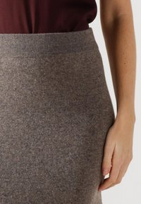 Gray wool blend skirt with a ribbed waistband. Soft texture, mid-length, featuring a subtle fleck pattern, shown with a dark top and hand.