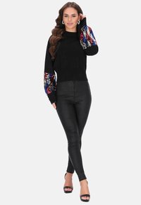 Černý svetr s dekorativními rukávy pokrytými flitry v červené, modré a stříbrné barvě. Spárováno s černými slim kalhotami a sandály na vysokém podpatku.